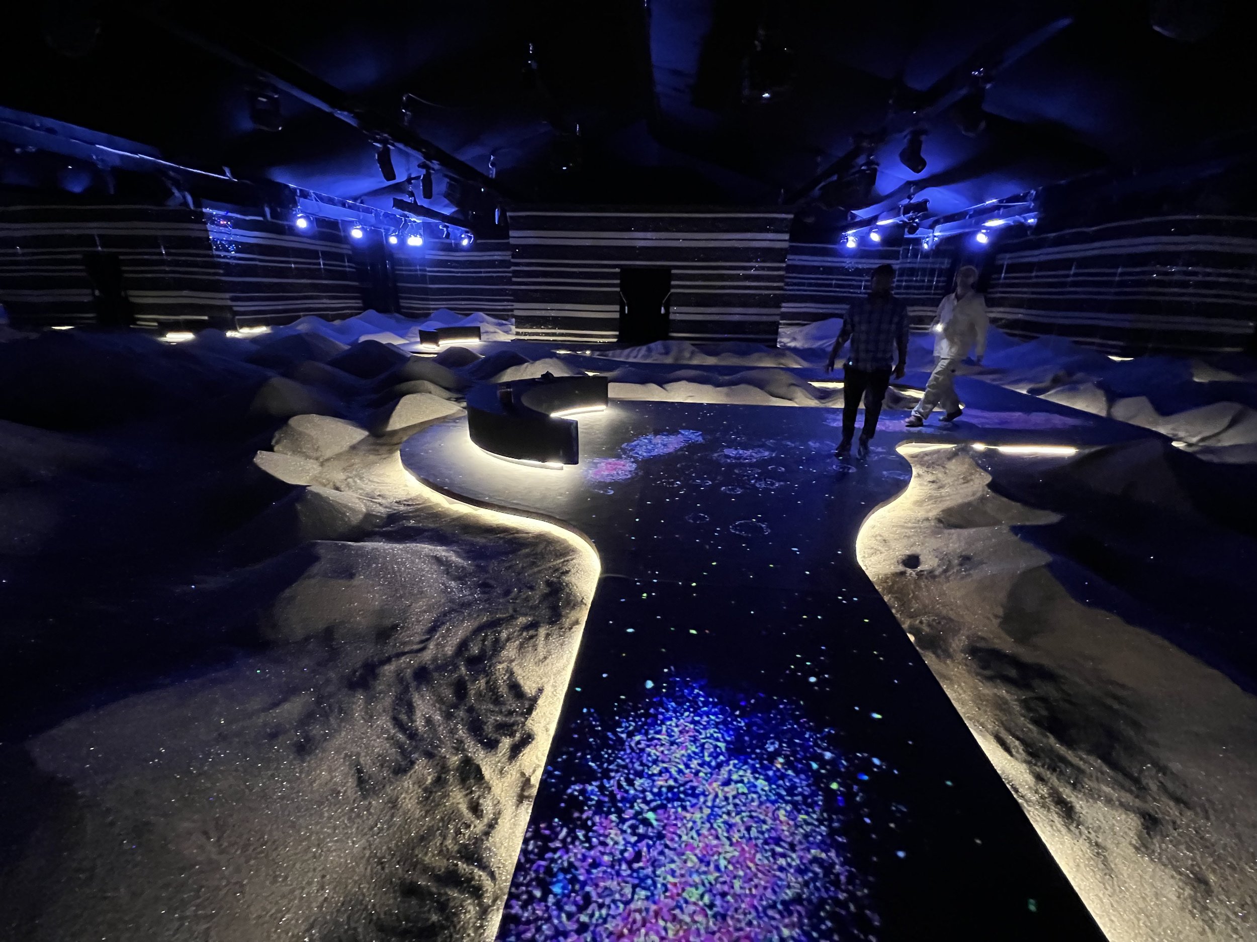 Indoor art installation featuring an interactive projection mapped walkway surrounded by mounds of sand covered with crystals.